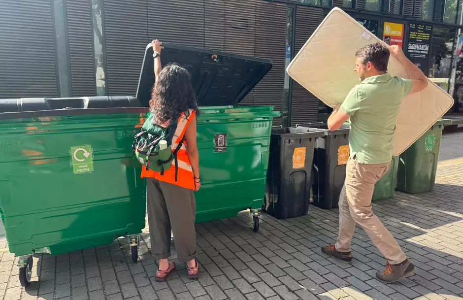 Man putting a mattress into a large communal bin during community skip day at Swiss Cottage